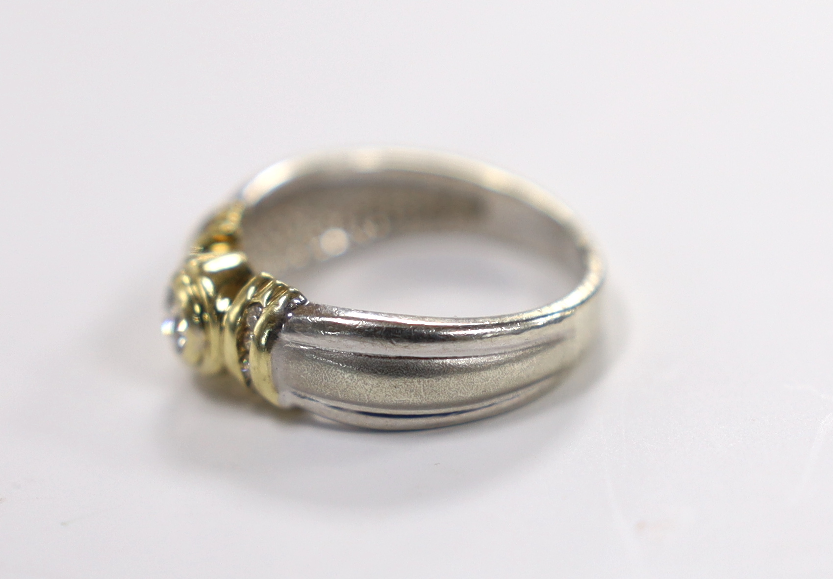 A modern two colour 9ct and collet set single stone diamond set ring, with diamond chip set shoulders, size N, gross weight 4.4 grams.